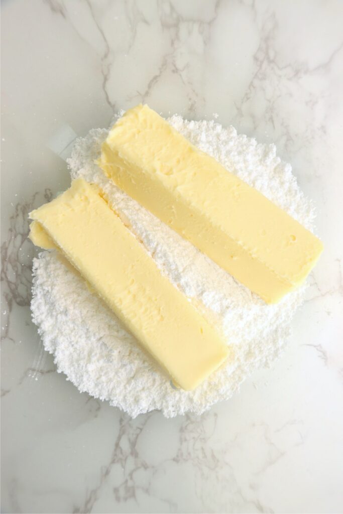 Overhead shot of two sticks of butter laying on top of powdered sugar