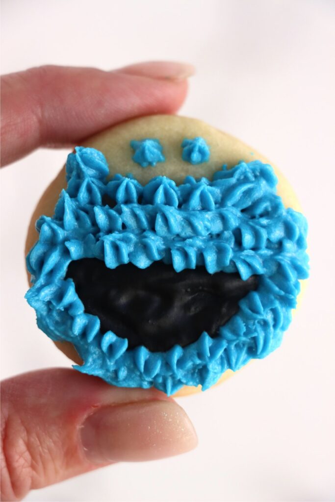 Closeup shot of hand holding cookie decorated with blue and black frosting. 