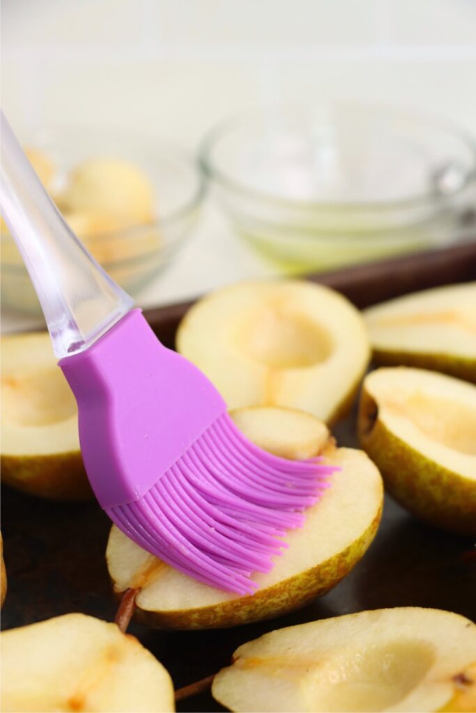 Closeup shot of cut pears on baking sheet being brushed with olive oil