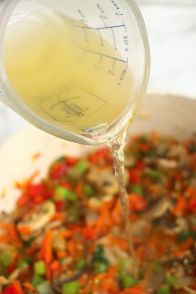 Closeup shot of chicken broth being poured into skillet with vegetables