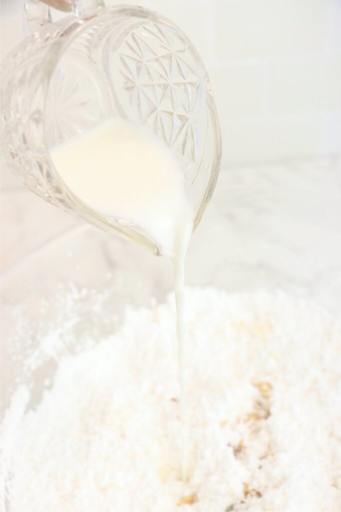 Milk being poured into butter and powdered sugar mixture in mixing bowl