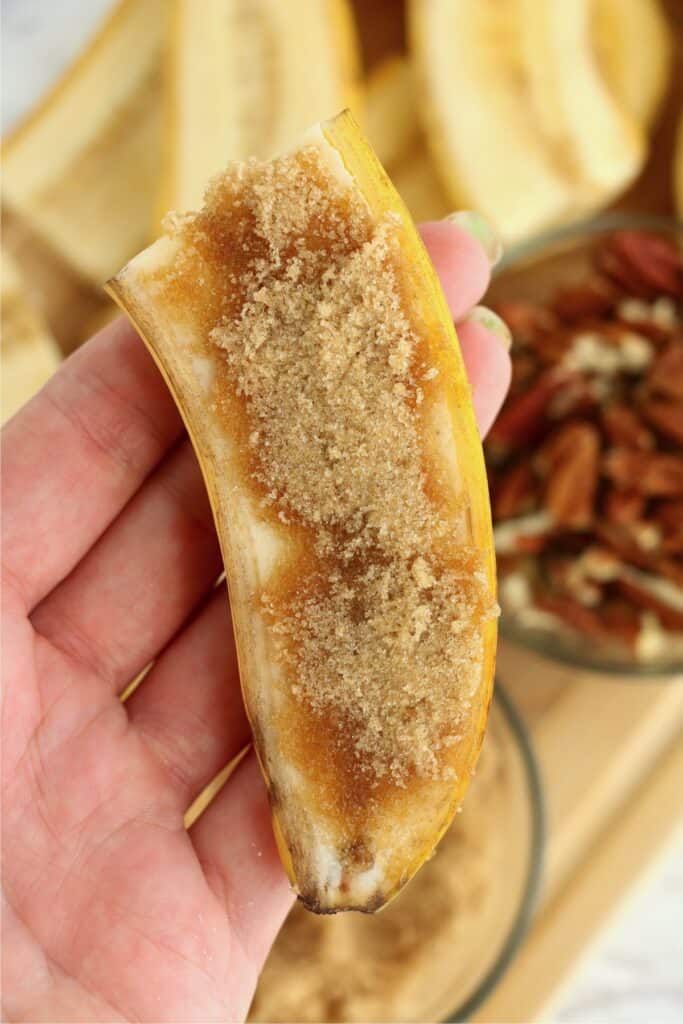 Closeup shot of hand holding a banana cut in half and topped with brown sugar.