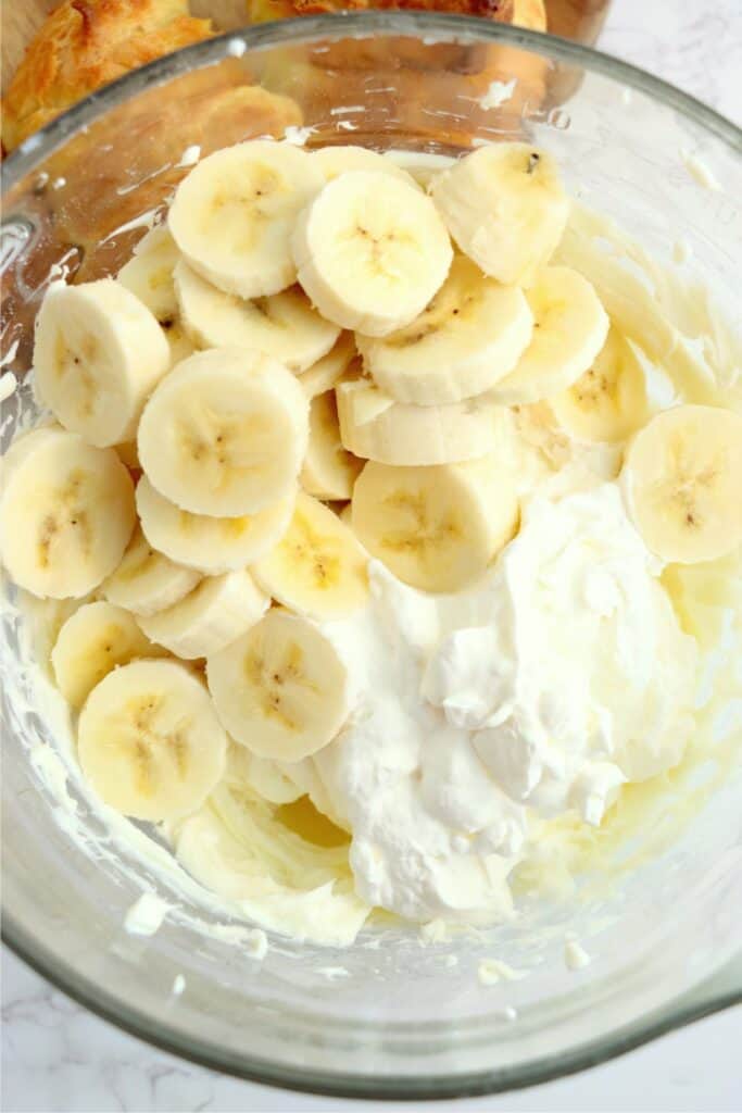 Overhead shot of whipped cream, sliced bananas, and cream cheese mixture in mixing bowl