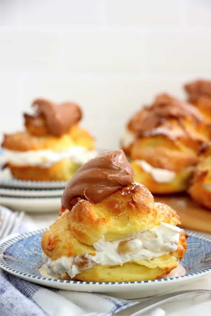 Banana cream puff on plate with more banana cream puffs in background.