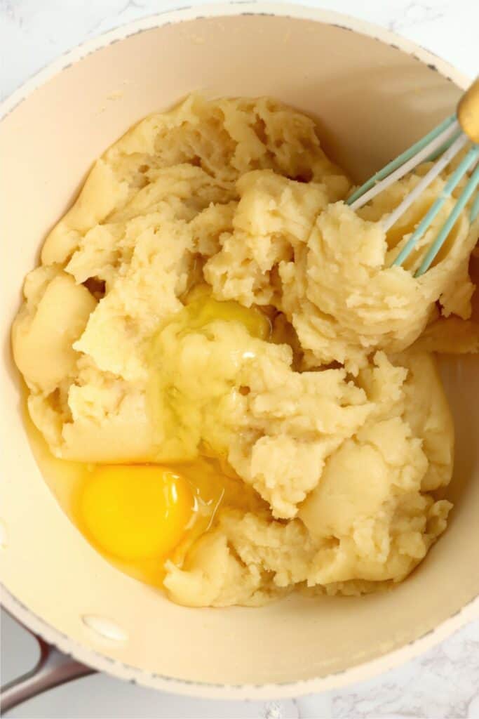 Closeup shot of eggs being mixed into cream puff dough in saucepan