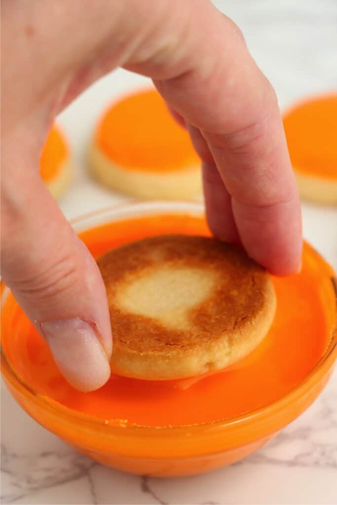 Closeup shot of the top of a sugar cookie being dipped into orange icing.