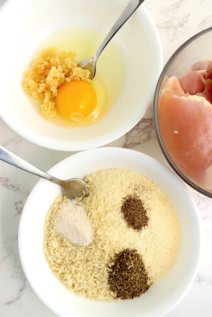 Overhead shot of a bowl with egg and garlic next to another bowl with breadcrumbs, parmesn, and spices