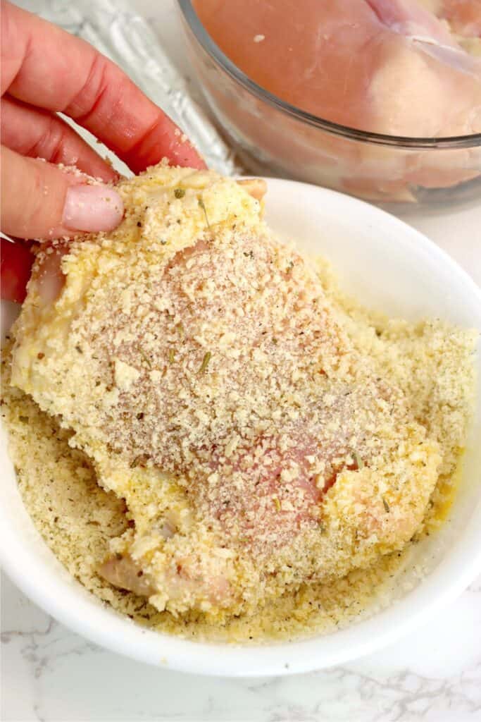 Hand coating a chicken thigh in breadcrumb mixture