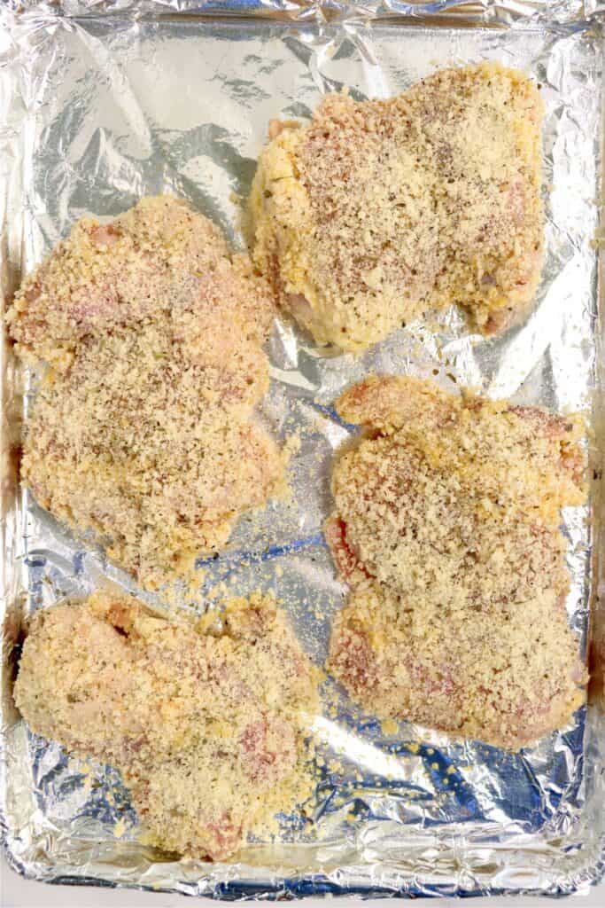 Overhead shot of raw garlic parmesan chicken thighs on baking sheet lined with foil