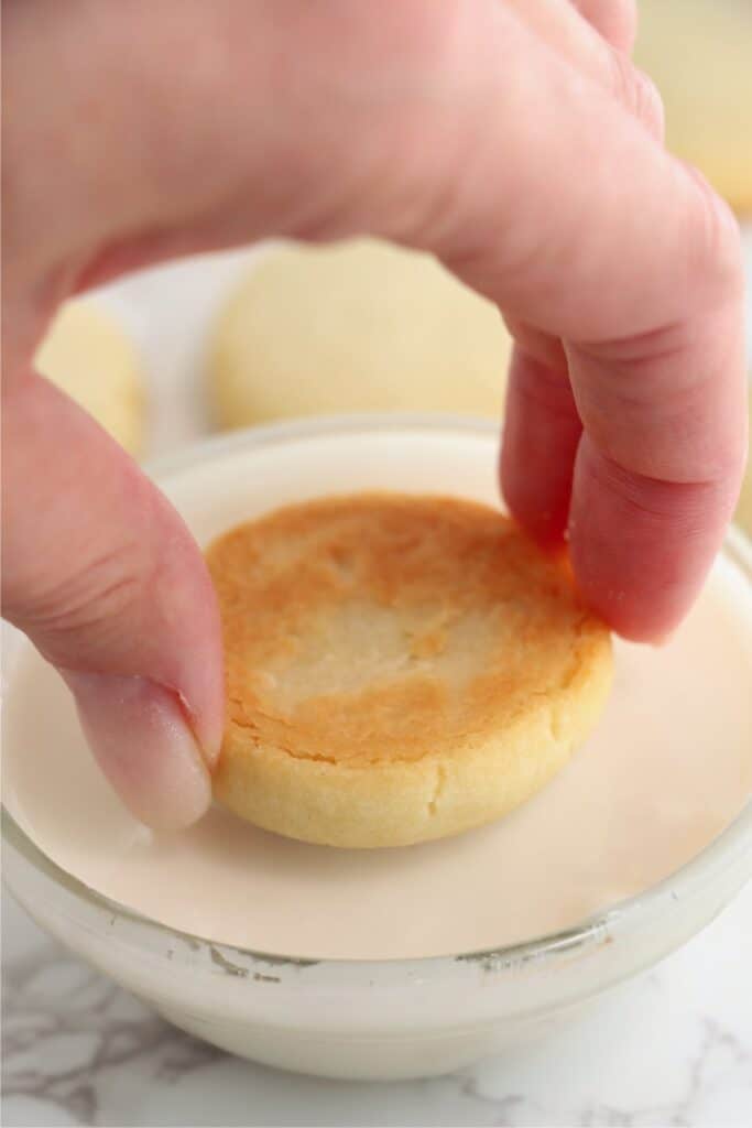 Closeup shot of hand dipping baked sugar cookie in bowl of icing.