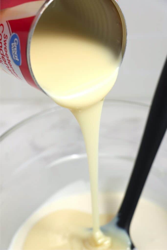 Sweetened condensed milk being poured into bowl of melted white almond bark