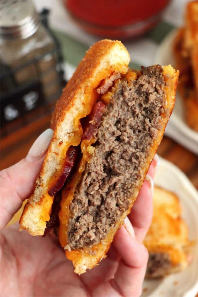 Closeup shot of hand holding half a grilled cheese bacon hamburger