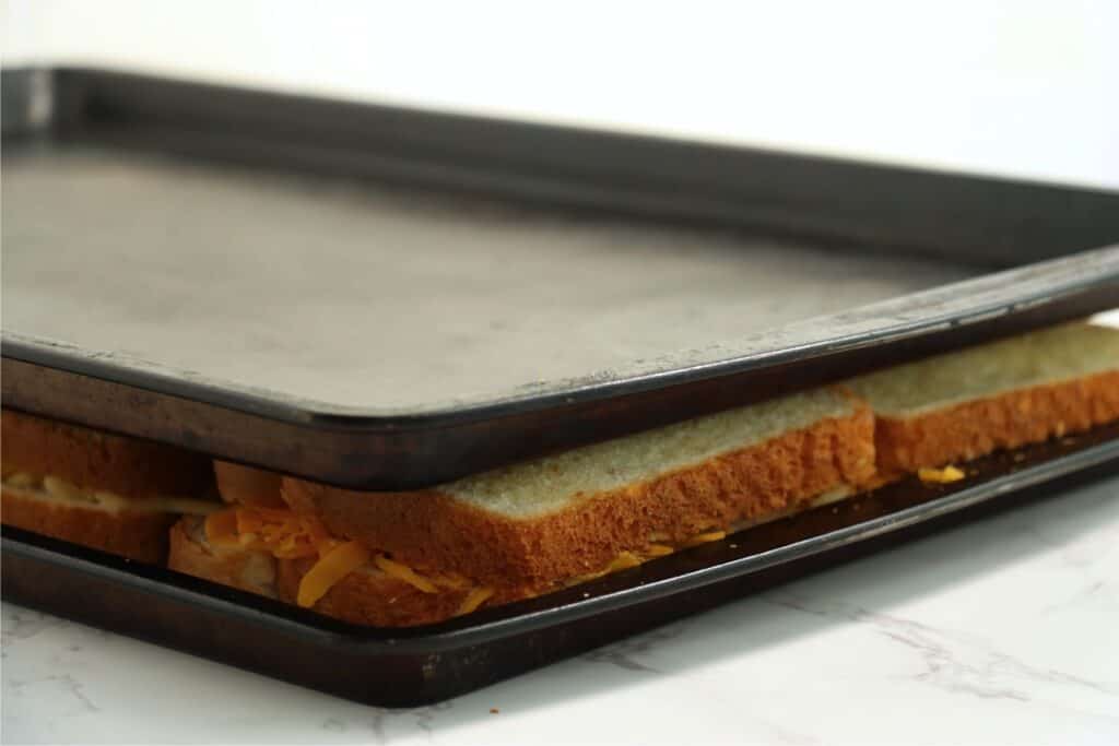 Grilled cheese sandwiches sandwiched between two baking sheets