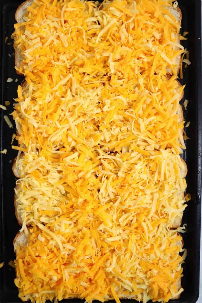 Overhead shot of bread slices topped with cheese on baking sheet