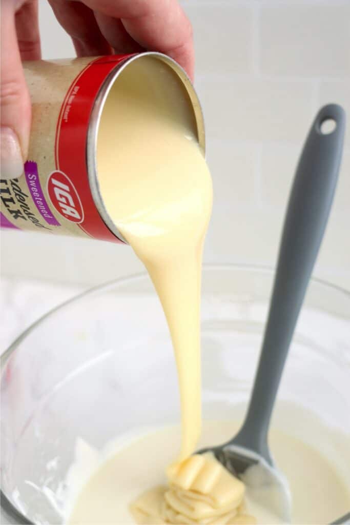 Sweetened condensed milk being poured into bowl of melted almond bark