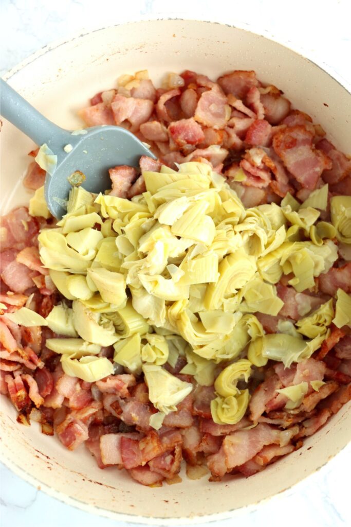 Overhead shot of artichoke hearts in skillet full of bacon, onion, and garlic.