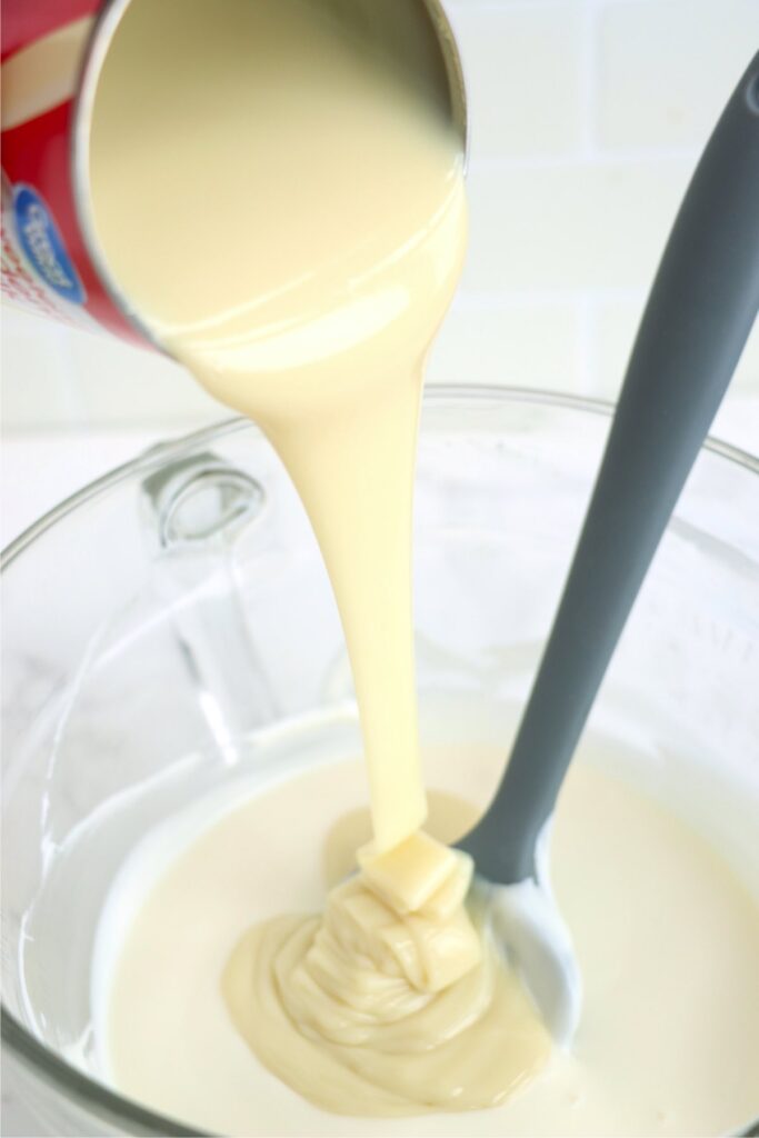 Sweetened condensed milk being poured into bowl of melted vanilla bark