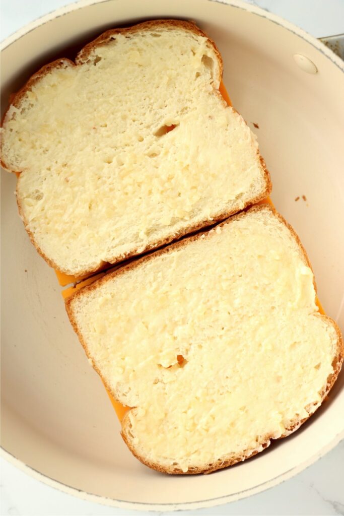 Overhead shot of uncooked garlic grilled cheese sandwiches in pan.