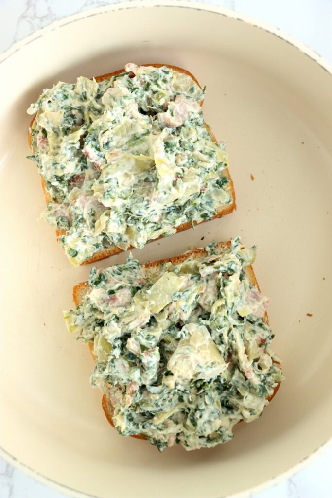 Overhead shot of two pieces of bread topped with spinach artichoke dip in skillet