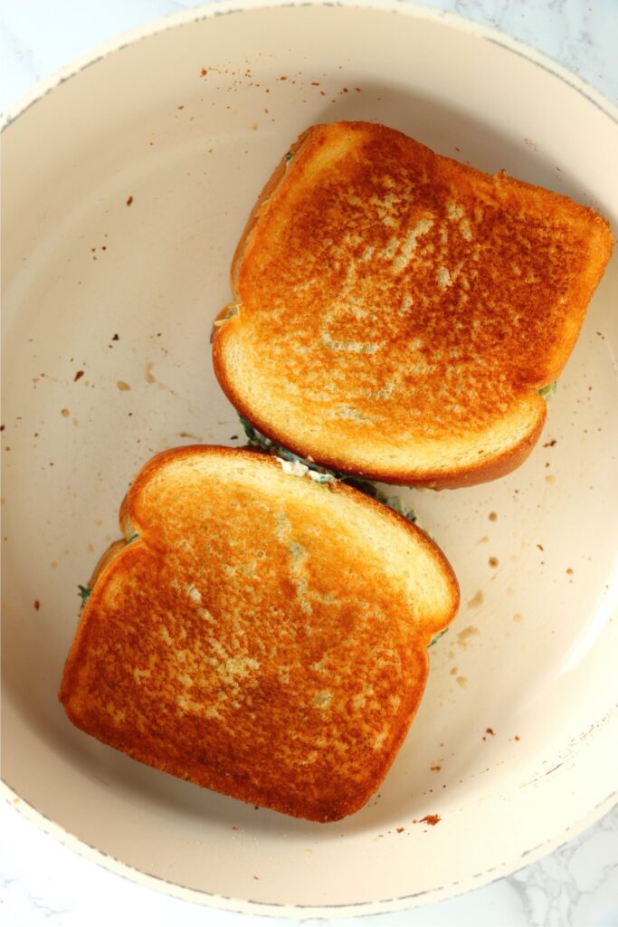 Overhead shot of two spinach artichoke grilled cheese sandwiches in skillet 