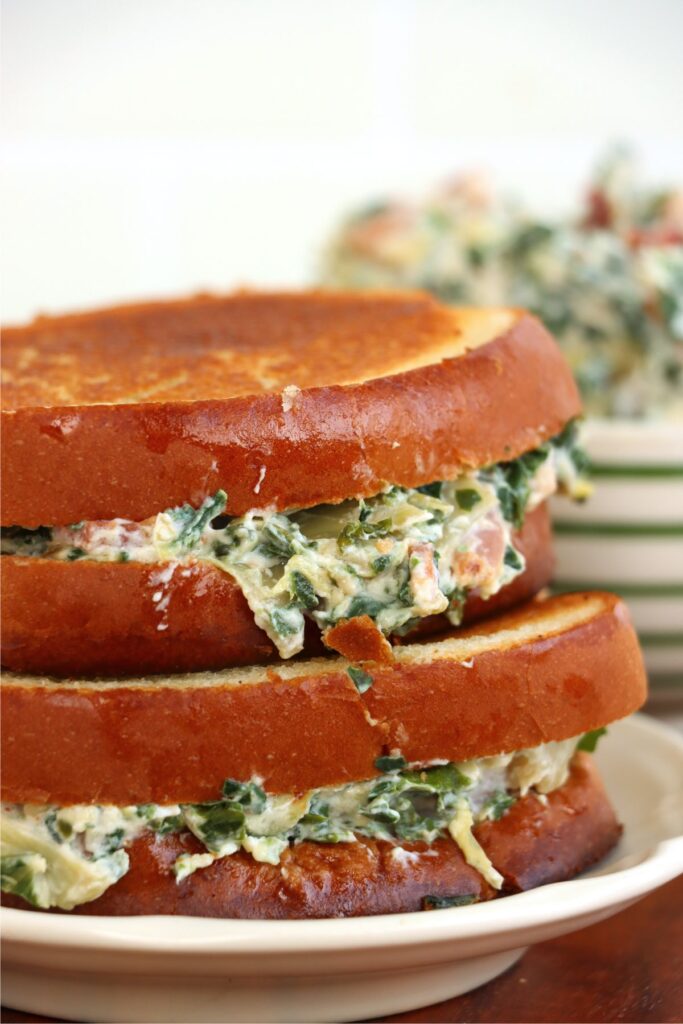 Closeup shot of two spinach artichoke grilled cheese sandwiches on plate.