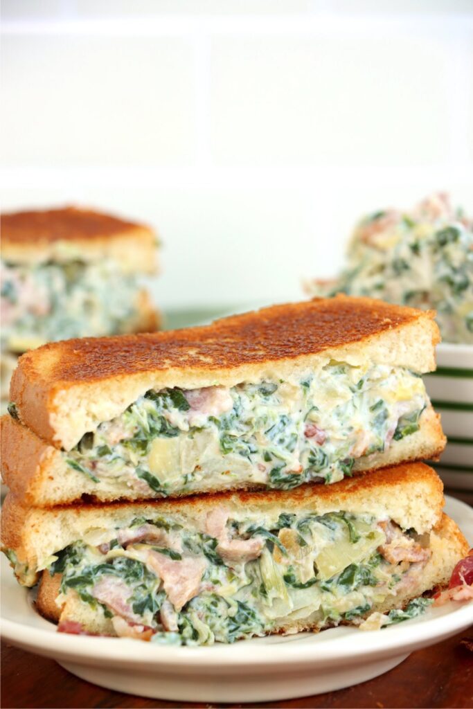 Two spinach artichoked grilled cheese sandwich halves stacked atop one another on plate.
