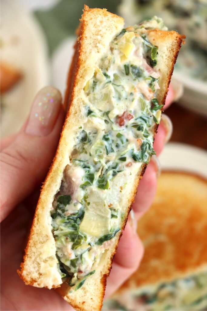 Closeup shot of hand holding half a spinach artichoke grilled cheese sandwich