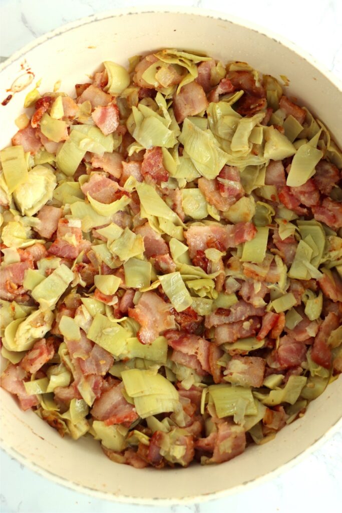 Overhead shot of panful of bacon, onions, garlic, and artichokes.