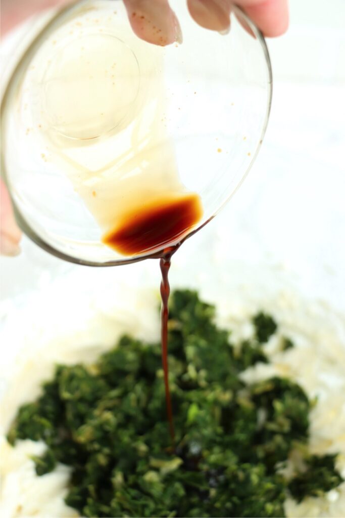 Worcestershire sauce being poured into bowl of spinach artichoke dip.