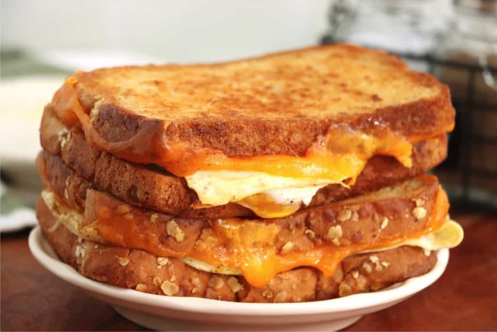 Two grille cheese and egg sandwiches stacked atop one another on plate.