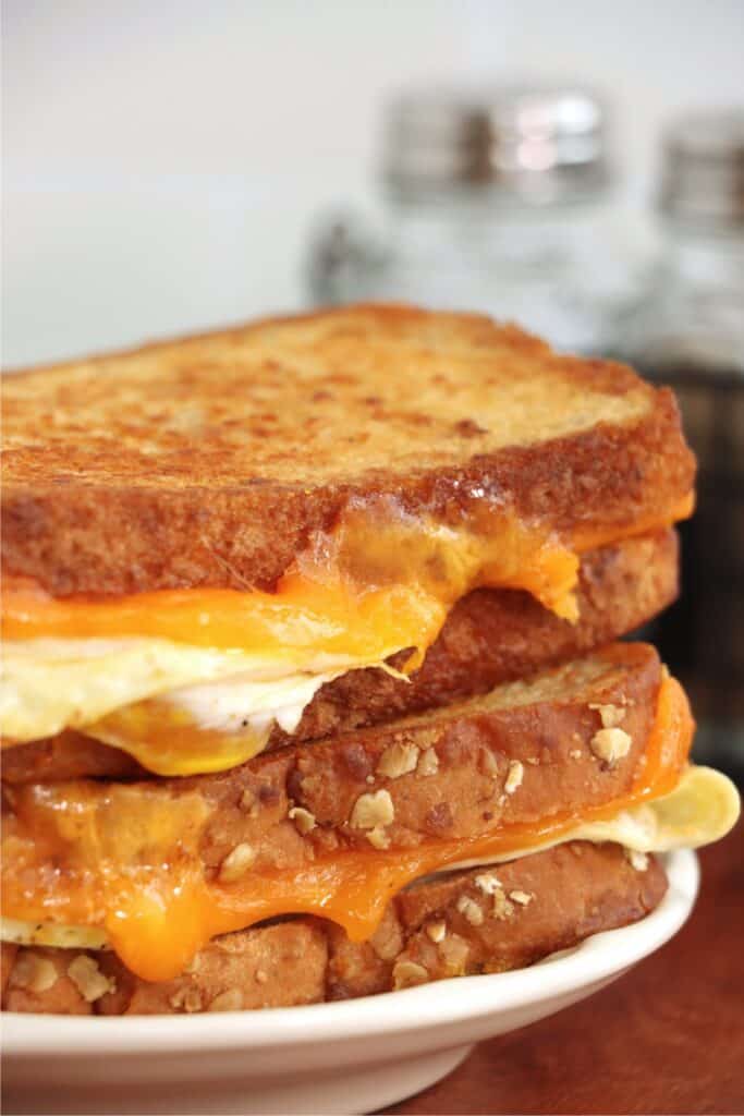 Grilled cheese and egg sandwiches stacked atop one another on plate