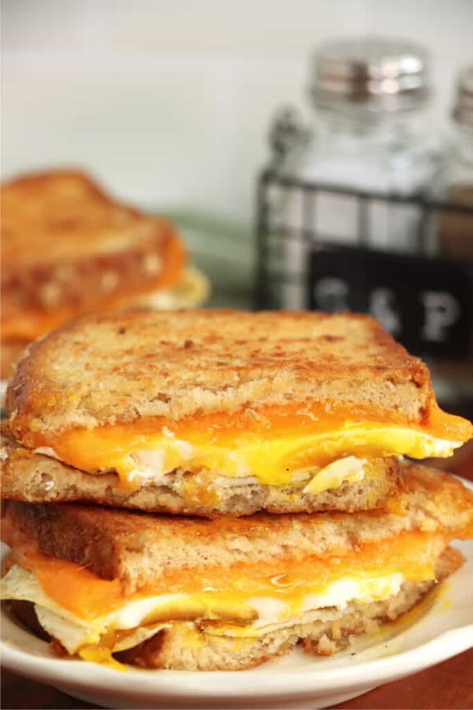 Closeup shof two grilled cheese and egg sandwiche halves stacked atop one another.