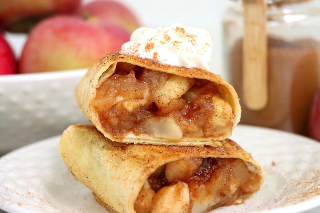 Closeup shot of homemade apple wraps topped with whipped cream on plate.