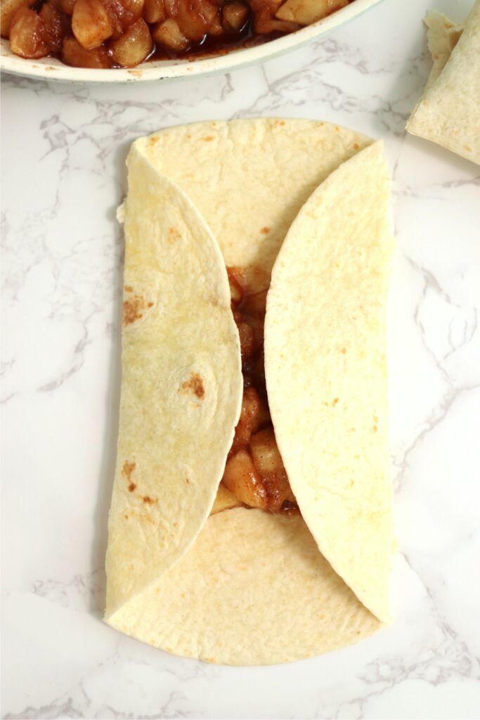 Overhead shot of tortilla being folded around apple filling