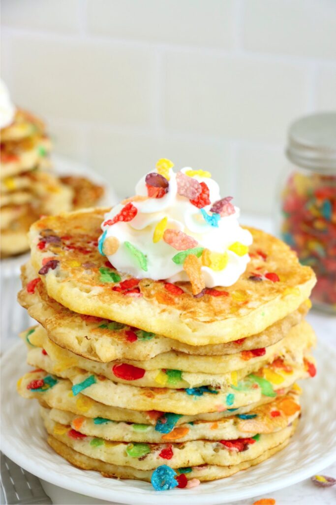 Stack of Fruity Pebbles pancakes topped with whipped cream on plate