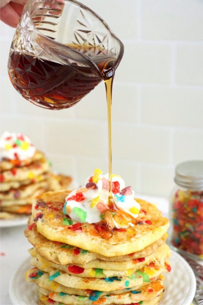 Sryup being drizzled over stack of Fruity Pebbles pancakes on plate