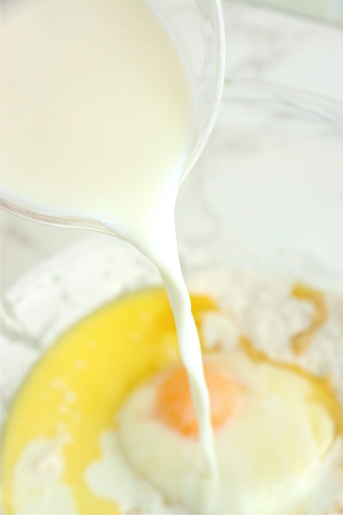 Milk being poured into bowlful of pancake batter ingredients