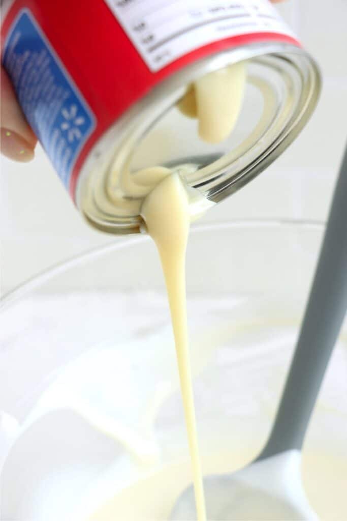 Closeup shot of sweetened condense milk being poured into bowl of melted almond bark