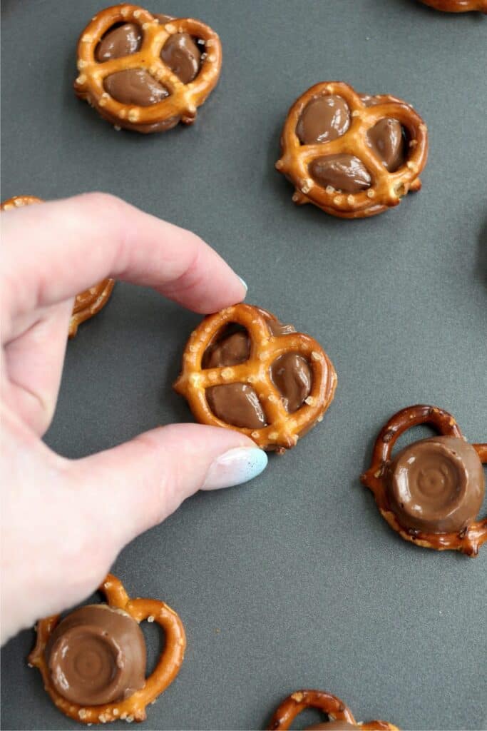 Overhead shot of hand pressing pretzel into melted Rolos on baking sheet