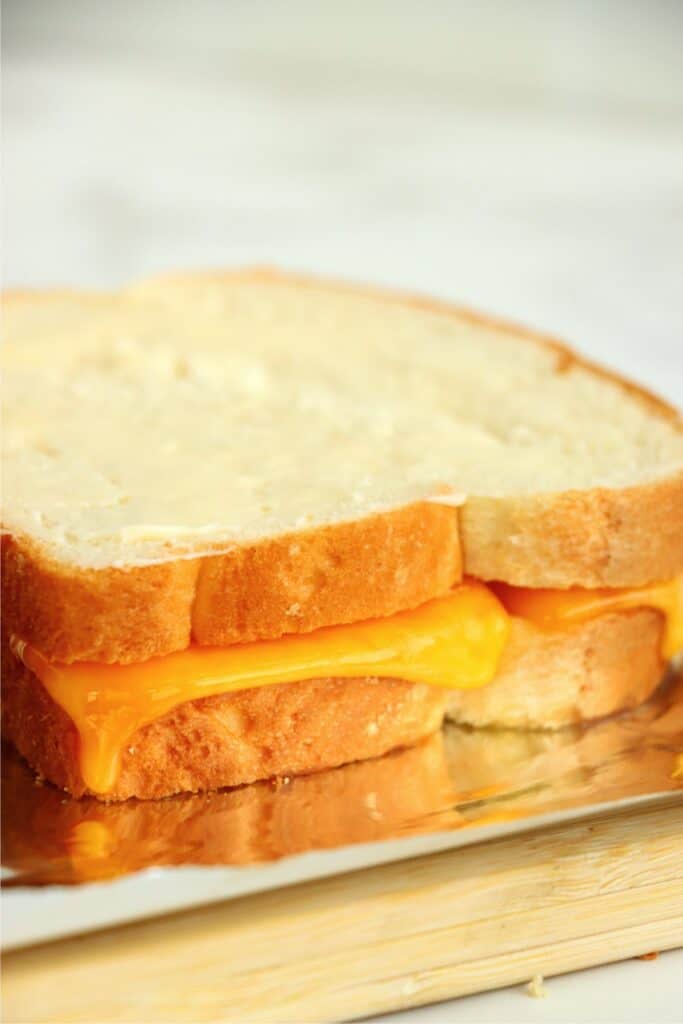 Closeup shot of partially melted grilled cheese with slice of buttered bread on top