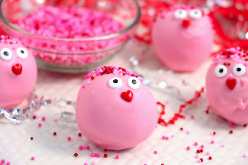 Closeup shot of Valentine Oreo truffles next to bowlful of pink sprinkles on table