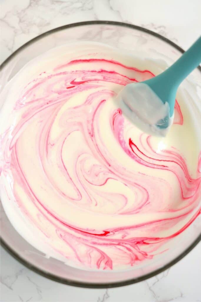 Closeup shot of white almond bark being mixed with pink food coloring in mixing bowl