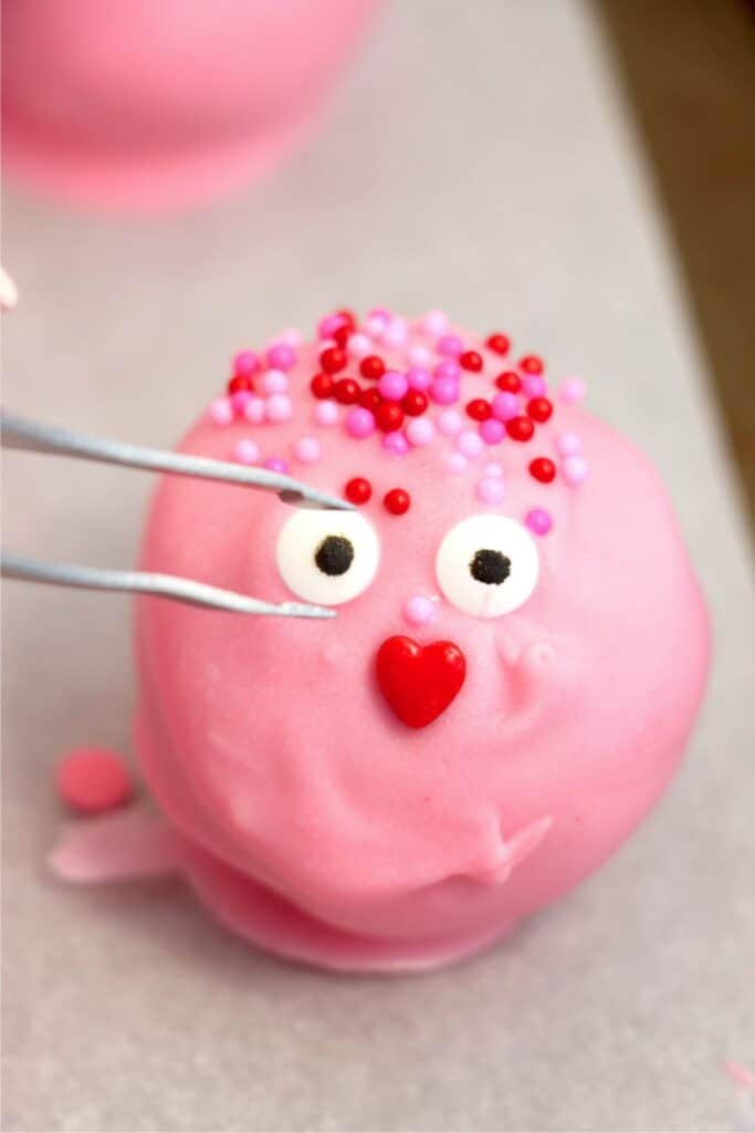 Closeup shot of Valentine Oreo truffle being decorated with sprinkles and googly eyes