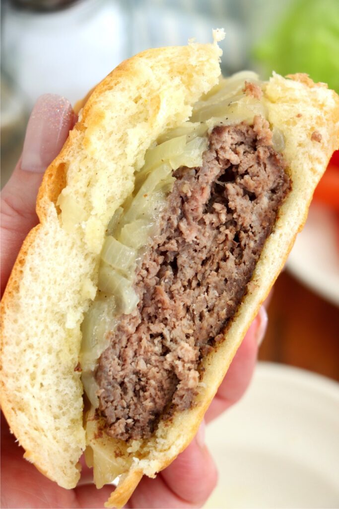 Closeup shot of hand holding half a grilled onion cheddar burger. 