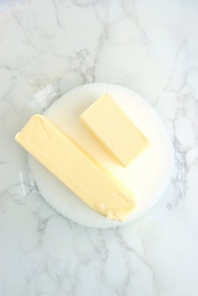 Closeup overhead shot of butter sticks and sugar in mixing bowl