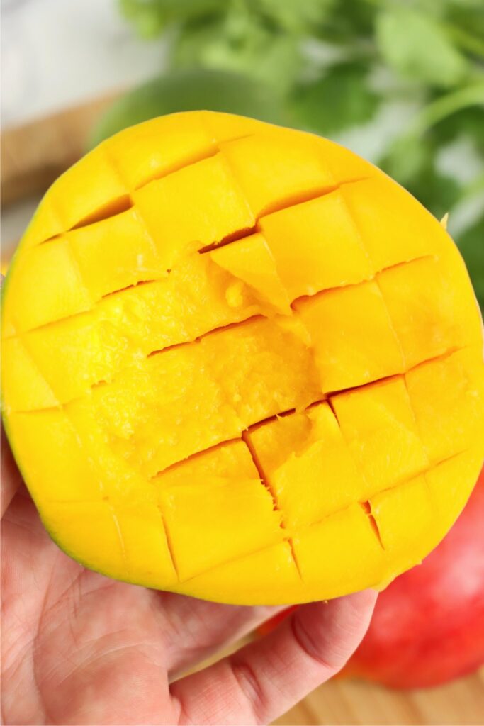 Closeup shot of hand holding a mango half that's been sliced.