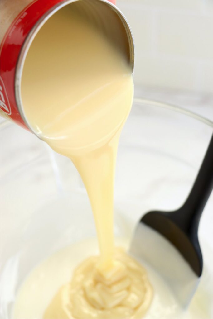 Sweetened condensed milk being poured into bowl of melted vanilla bark