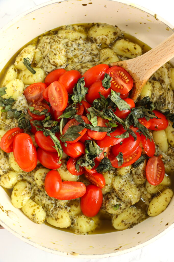 Overhead shot of tomatoes and fresh basil being stirred into gnocchi mixture.