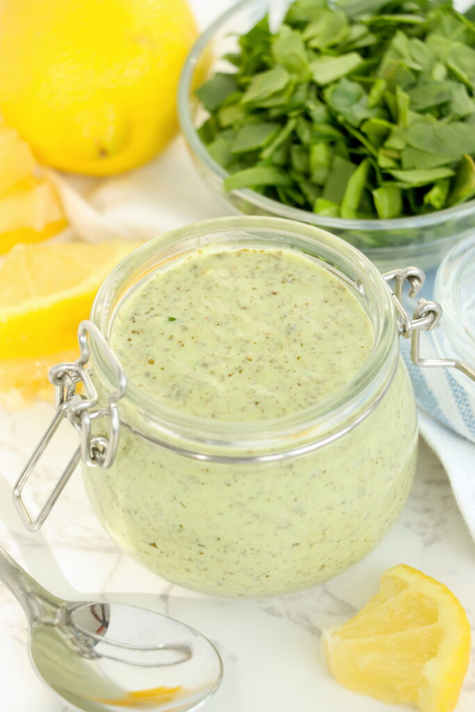 Closeup shot of pesto mayo in glas jar next to bowlful of chopped basil