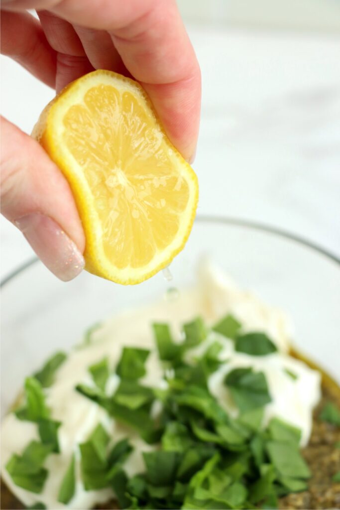 Closeup shot of lemon juice being squeezed into bowl of pesty mayo recipe ingredients